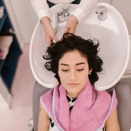Dunkelhaarige Frau welcher die Haare beim Friseur im Waschbecken gewaschen werden
